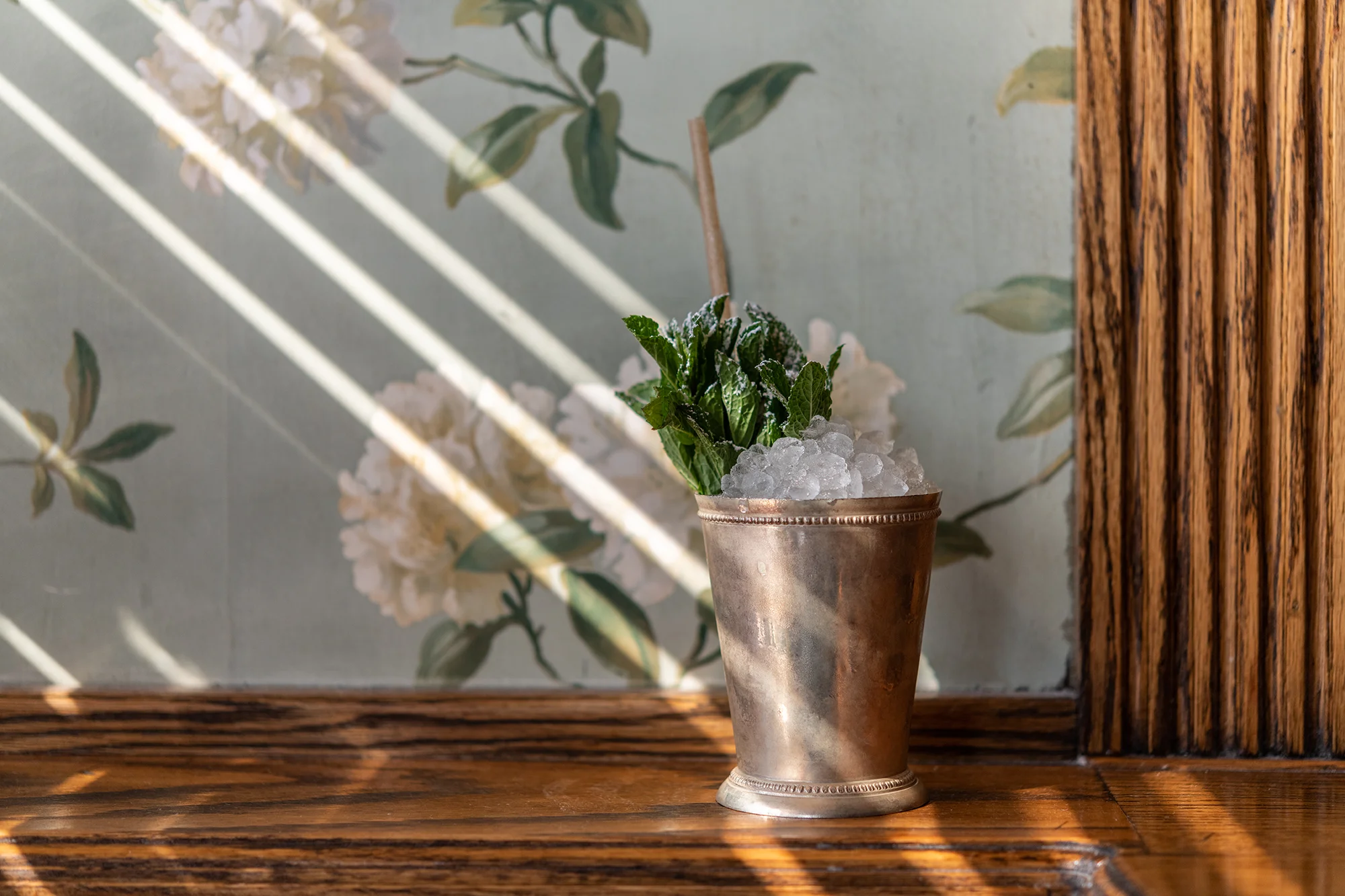 A copper cup with ice and Mint in front of floral wallpaper